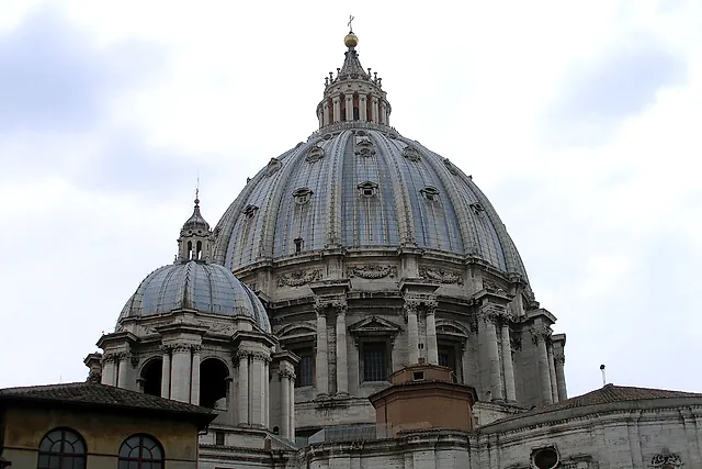 Michelangelo's great dome of St Peter's Basilica rising above the rooftops of the Vatican under a blue sky